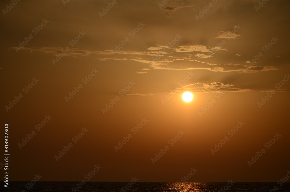 Beautiful sunset sky and a small ball of sun setting over the horizon above the sea surface