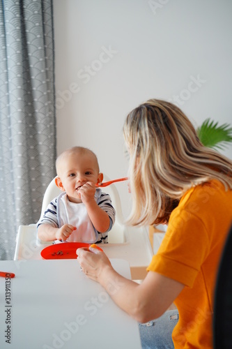 Mom feeding her baby girl with a spoon. Mother giving food to her eight-month child at home.
