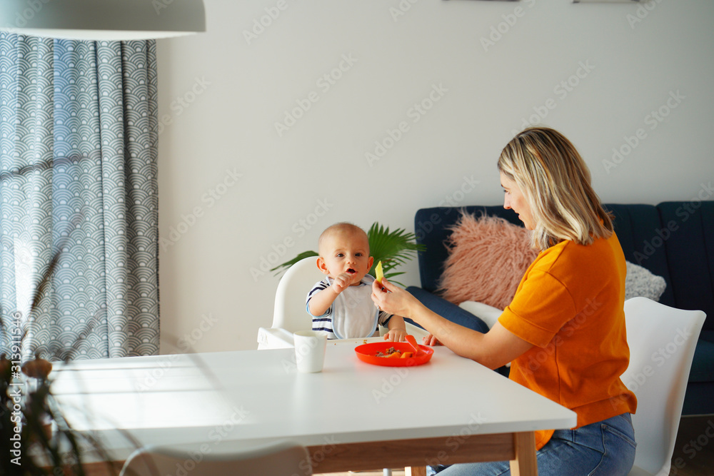 Mom feeding her baby girl with a spoon. Mother giving food to her eight-month child at home.