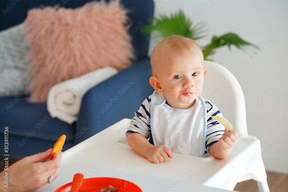 Mom feeding her baby girl with a spoon. Mother giving food to her eight-month child at home.