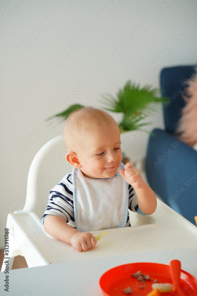 Mom feeding her baby girl with a spoon. Mother giving food to her eight-month child at home.