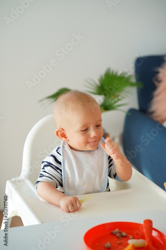 Obraz na płótnie Mom feeding her baby girl with a spoon. Mother giving food to her eight-month child at home. w salonie