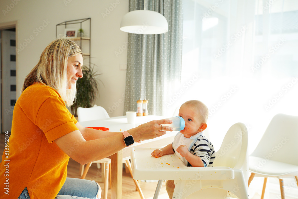 Mom feeding her baby girl with a spoon. Mother giving food to her eight-month child at home.