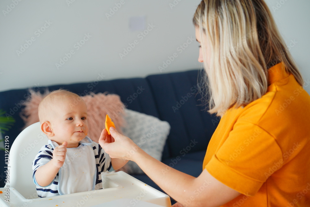 Mom feeding her baby girl with a spoon. Mother giving food to her eight-month child at home.