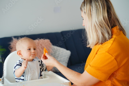 Obraz na płótnie Mom feeding her baby girl with a spoon. Mother giving food to her eight-month child at home. w salonie