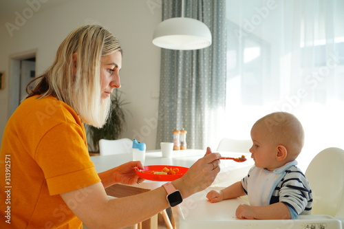 Obraz na płótnie Mom feeding her baby girl with a spoon. Mother giving food to her eight-month child at home. w salonie