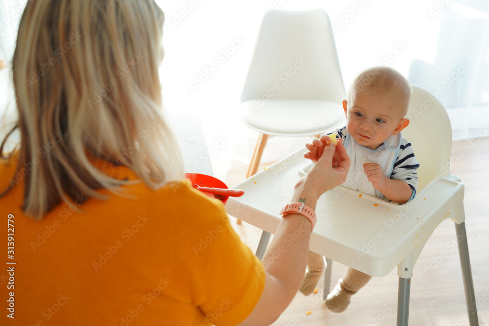 Mom feeding her baby girl with a spoon. Mother giving food to her eight-month child at home.