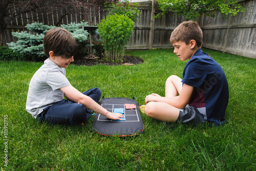 Two young boys playing a tic tac toe game in the backyard together.