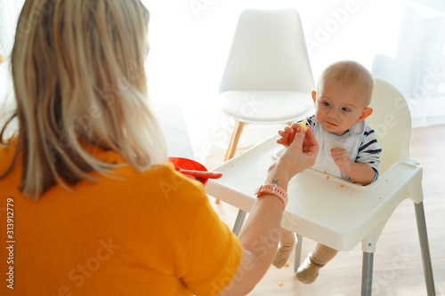 Obraz na płótnie Mom feeding her baby girl with a spoon. Mother giving food to her eight-month child at home. w salonie