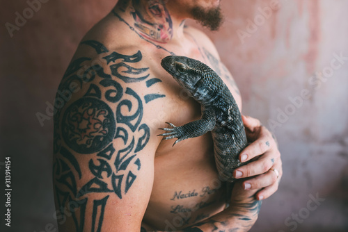 tattooed and shirtless man hugs a lizard Varanus exanthematicus photo