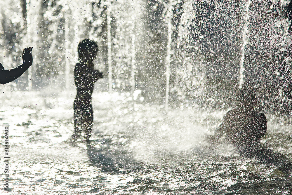 Silhouette of kids cooling down in a fountain during heatwave Silhouette of kids cooling down in a fountain during heatwave