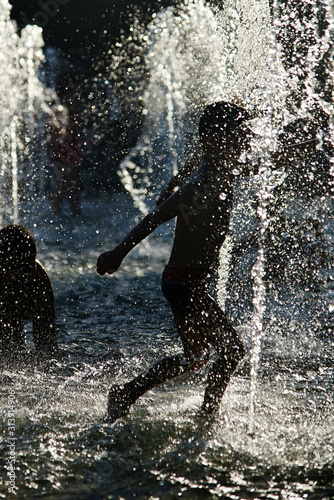 Silhouette of kids cooling down in a fountain during heatwave photo