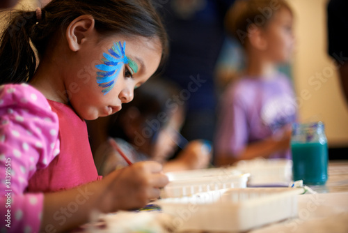 Profile view of a young Asian girl painting in art class