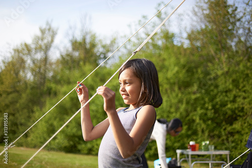 Young Asian girl playing with tent lines on a camping site photo