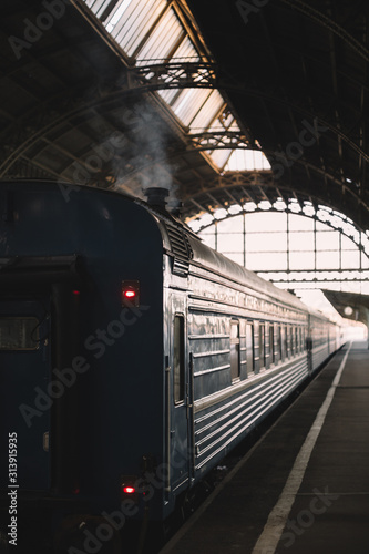 Retro passenger railway wagon preparing to depart from the covered platform. Smoke escapes from the chimney. Exterior of vintage railcar of train. Vertical photo. Vacation and tourism concept.