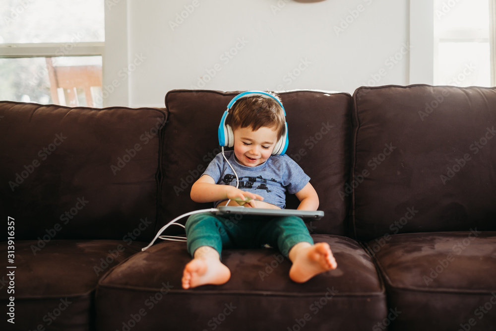 Young boy smiling playing with tablet on couch in livingroom Young boy smiling playing with tablet on couch in livingroom
