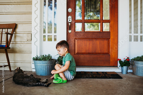 Young boy sitting outside front door petting short hair cat