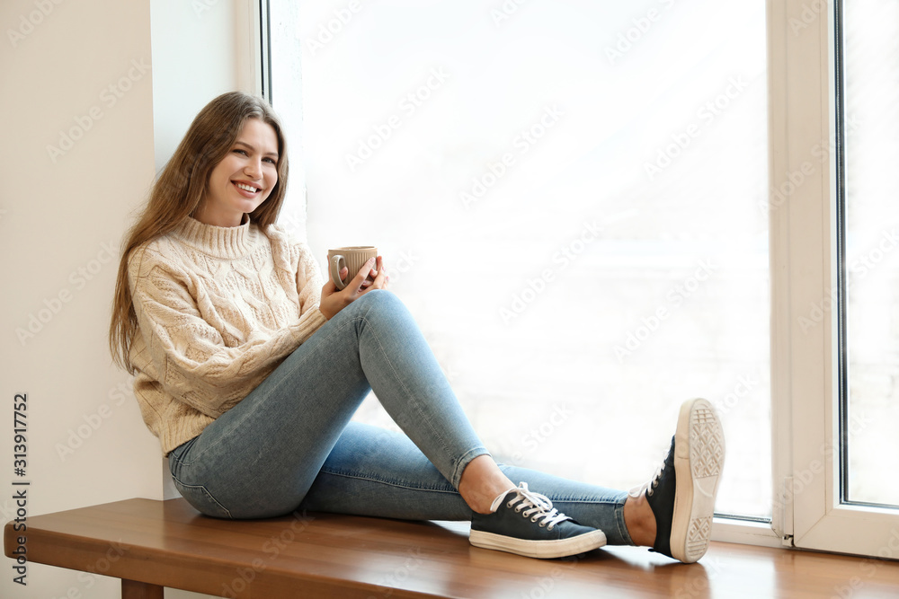 Young woman drinking hot tea on window sill at home Young woman drinking hot tea on window sill at home