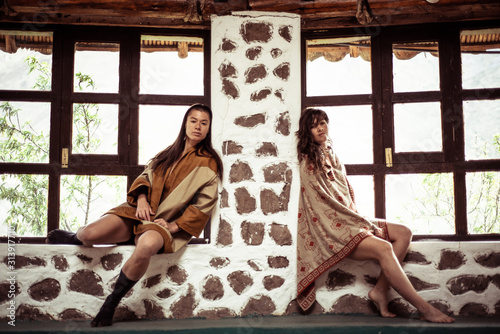 Same sex lesbian couple lean on stone wall in outdoor studio photo