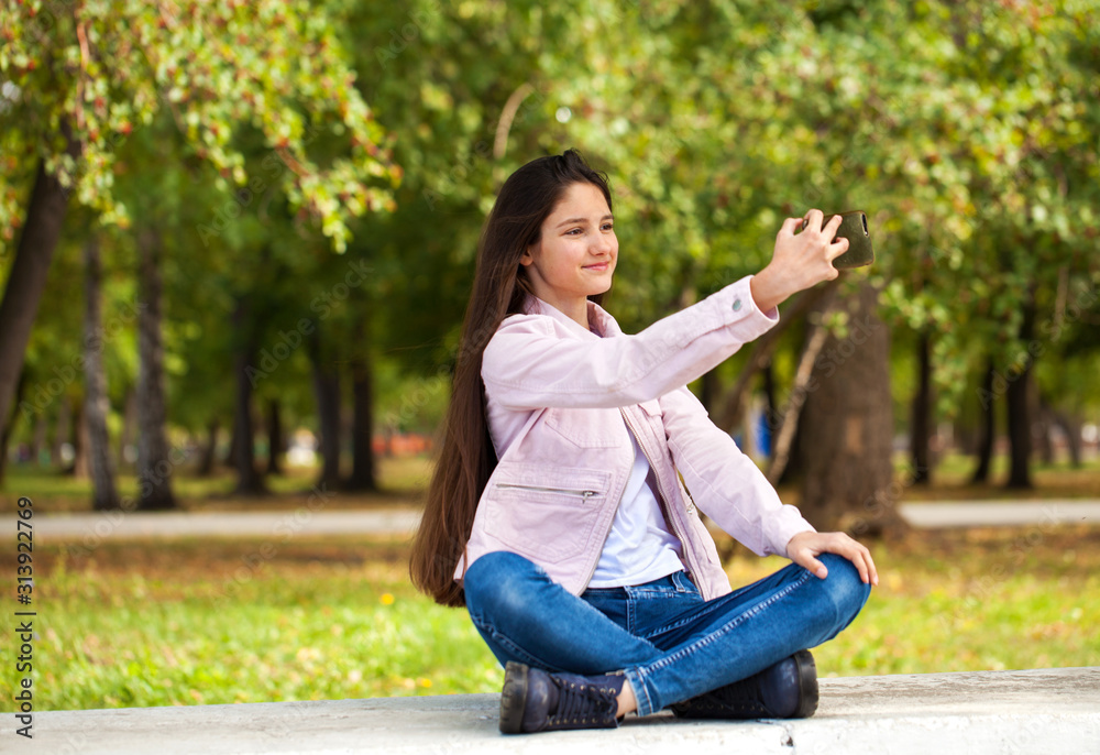 Brunette girl photographs herself on a cell phone while sitting in an autumn park. Brunette girl photographs herself on a cell phone while sitting in an autumn park.