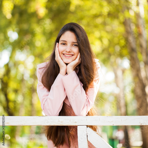 Portrait of a young brunette girl in pink coat on a background of autumn park photo