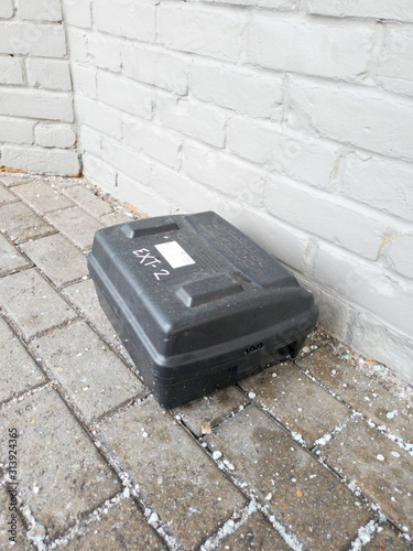 Black case on a dirty walkway beside a brick building.