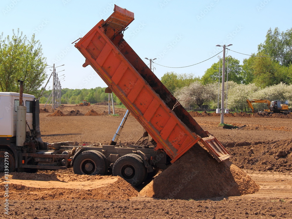 Power tipper truck unload sand from dump bed at the construction site on Sunny summer day