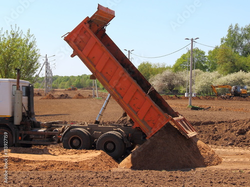 Obraz na płótnie Power tipper truck unload sand from dump bed at the construction site on Sunny summer day w salonie