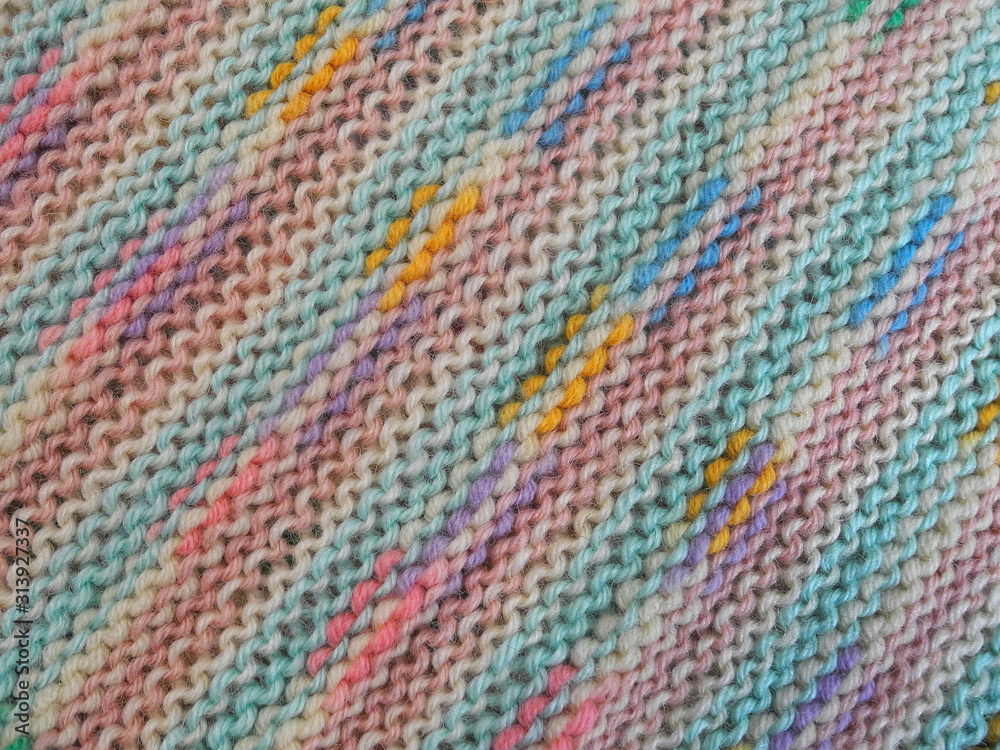 Background of handmade knitted fabric made of motley melange wool yarn closeup