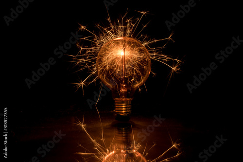 Electric tungsten lightbulb on a black background emitting sparks