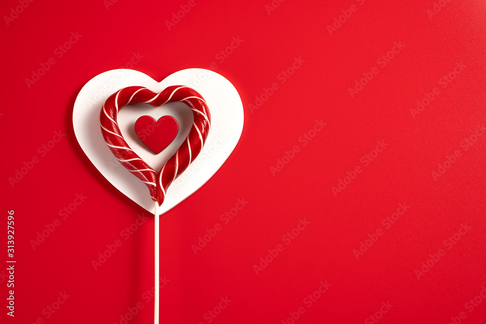 Heart-shaped Lollipop with red hearts on a white wooden heart on a red background for Valentine's Day, wedding and other holidays, view from the top.