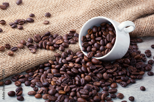 Coffee beans on light wooden background. Roasted coffee beans  white cup  sackcloth  can be used as a background