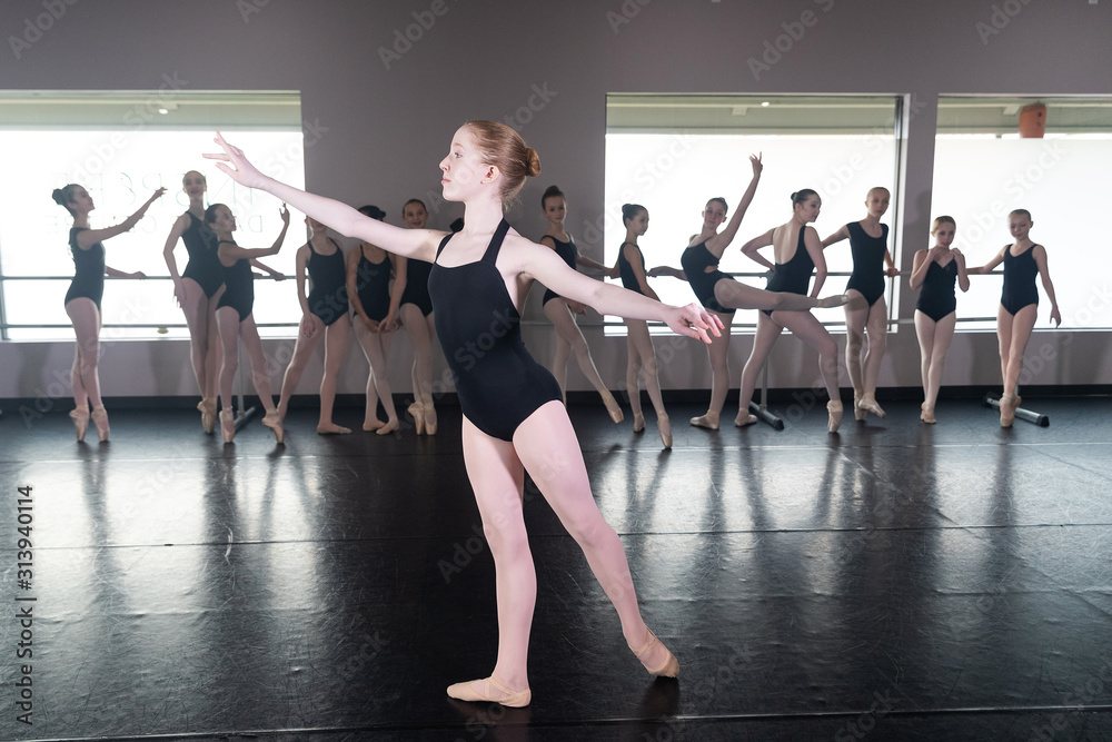 Teenage girl in ballet dance studio poses with the rest of the class behind her