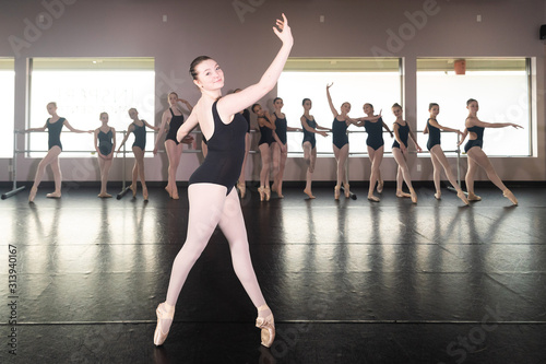 Teenage girl in ballet dance studio poses with the rest of the class behind her