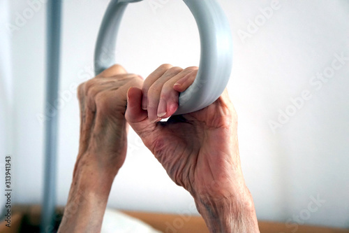 Hände einer Seniorin am Haltegriff eines Pflegebettes photo