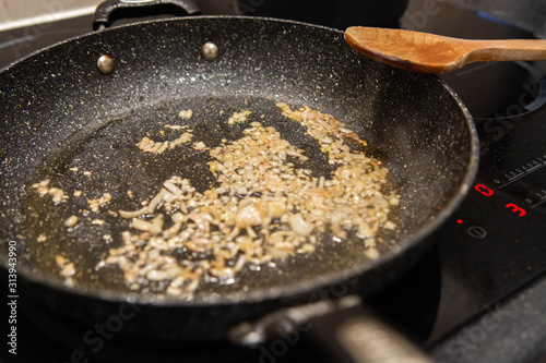 Closeup of shallots frying in a pan with a wooden spoon on a modern hob. 