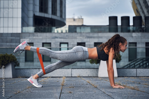 Young athletic woman doing exercises with sports rubber at the urban city location