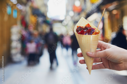 Woman hand holding paper cone with take away jamon on a street of San Sebastian, Spain
