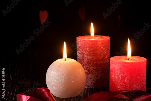 Three wax flame candlelight with ribbon in dark romantic light on hearts background  love dating  Valentine s day  selective focus