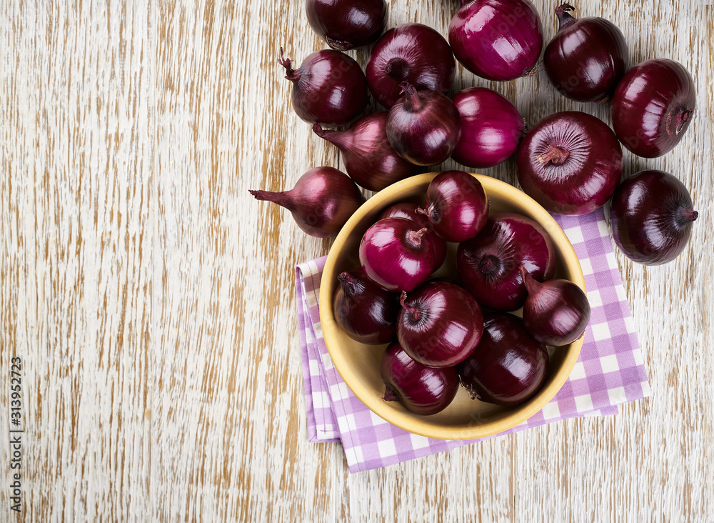 Red onions in wooden bowl on wooden background. Top view. Red onions in wooden bowl on wooden background. Top view.