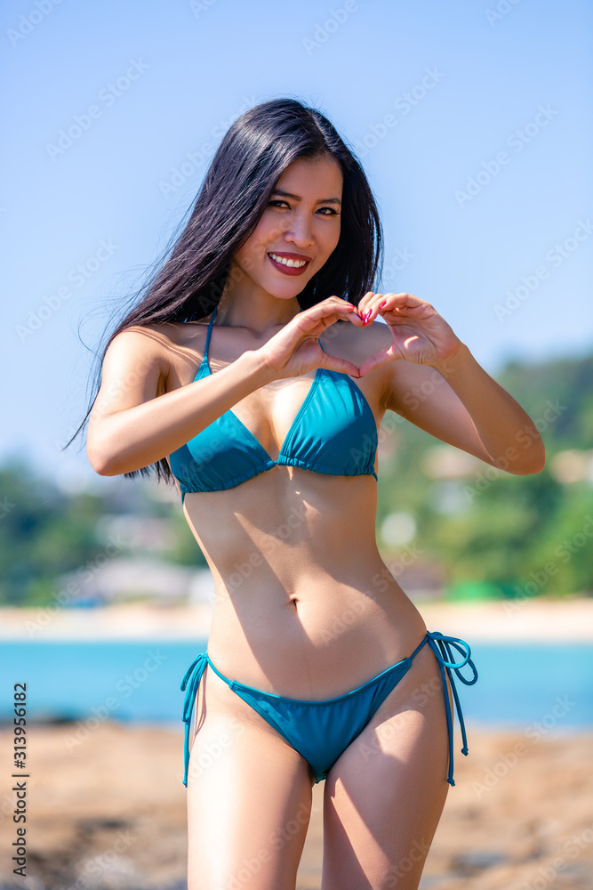 Beautiful asian girl in a blue bikini posing on a beach with rocks Stock  Photo | Adobe Stock
