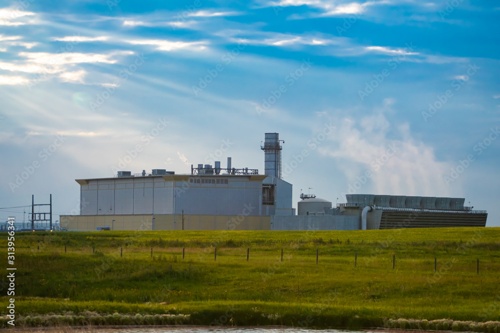 A large industrial complex is seen surrounded by rural countryside, with warehouse, tower and chimneys, under a blue sky with copy space A large industrial complex is seen surrounded by rural countryside, with warehouse, tower and chimneys, under a blue sky with copy space