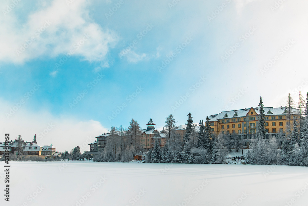 winter time hotel skying resort apartment buildings frozen lake and forest white snowy season scenic environment with cloudy blue sky background, copy space