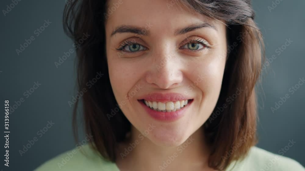 Close-up slow motion portrait of cheerful young lady smiling on dark background looking at camera with carefree face and nice smile. Modern youth and people concept. Close-up slow motion portrait of cheerful young lady smiling on dark background looking at camera with carefree face and nice smile. Modern youth and people concept.