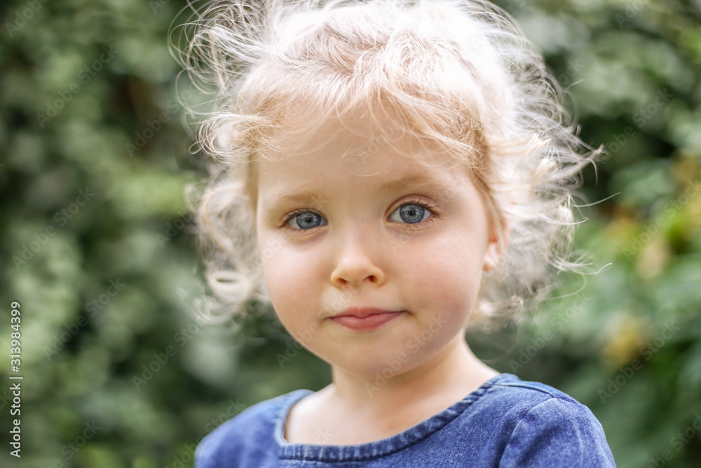 Portrait of a little beautiful European girl with curly blonde hair and blue eyes of 3 to 4 years in a classic blue color dress, trendy color 2020. Girl plays in the garden outside in spring or summer Portrait of a little beautiful European girl with curly blonde hair and blue eyes of 3 to 4 years in a classic blue color dress, trendy color 2020. Girl plays in the garden outside in spring or summer