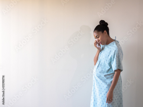 A young postpartum mixed race African American woman wearing a hospital gown or robe hunches over and looks down as she dries her eyes from tears of sadness or depression from a loss.