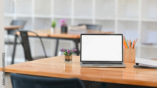 Front view Photo of white blank screen laptop on working desk. Including pencil holder, document files and potted plant on the work desk.