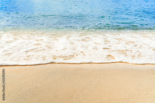 Ocean wave on tropical beach with golden sand and ripple of water splash from emerald blue-green sea water during summer vacation.