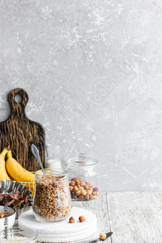 Chocolate banana granola with nuts in a glass jar on a light background