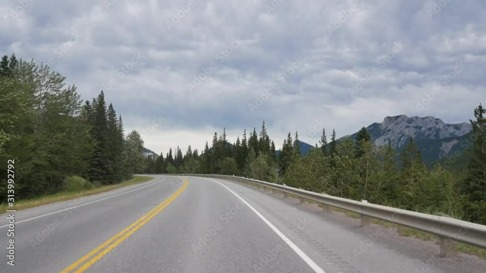 POV Landscape view from the moving car while driving along the local natural way in canada with natural view of Mountain range and pine tree forest in summer holiday/POV from front car POV Landscape view from the moving car while driving along the local natural way in canada with natural view of Mountain range and pine tree forest in summer holiday/POV from front car